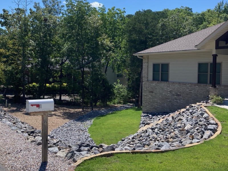 Front yard after — established sod lawn with a river-rock dry creek and clean stone borders